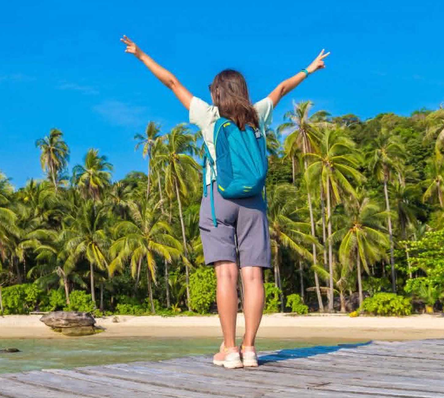 Voyageuse bras levés sur un ponton face à une plage tropicale
